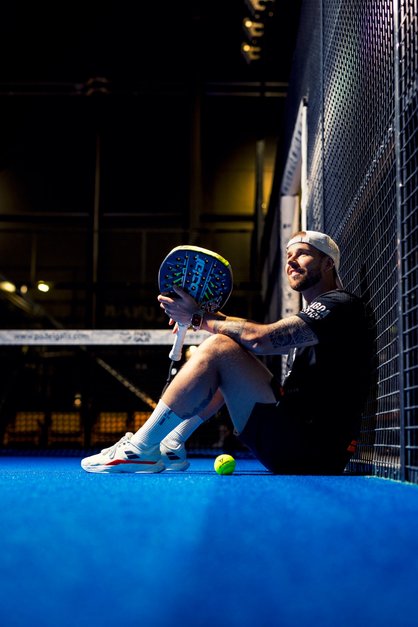 Frederik Sangill sitting against the fence of a blue padel court with a Babolat racket